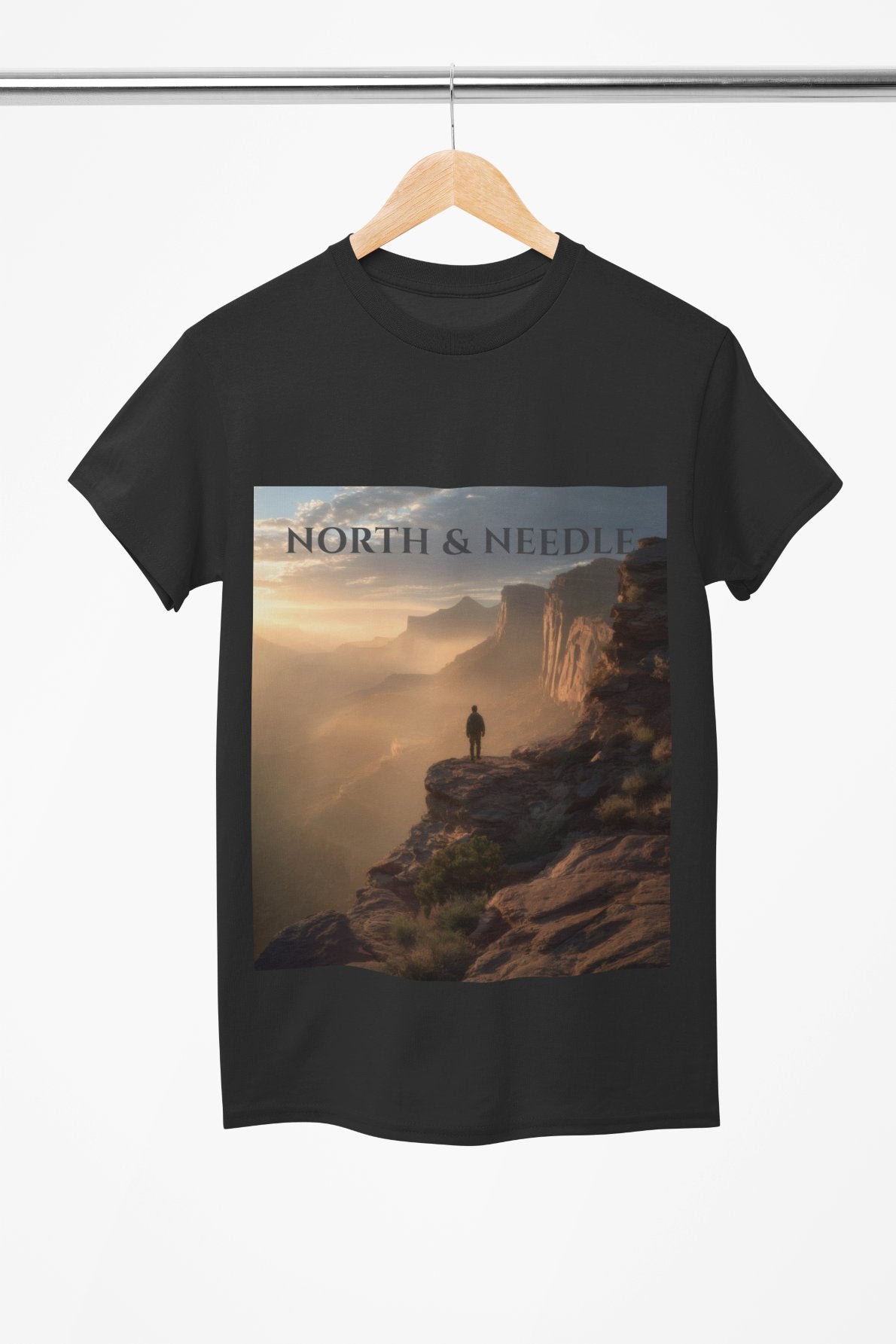 Black t-shirt with a scenic design of a person on a cliff and 'North & Needle' text, hanging on a wooden hanger.