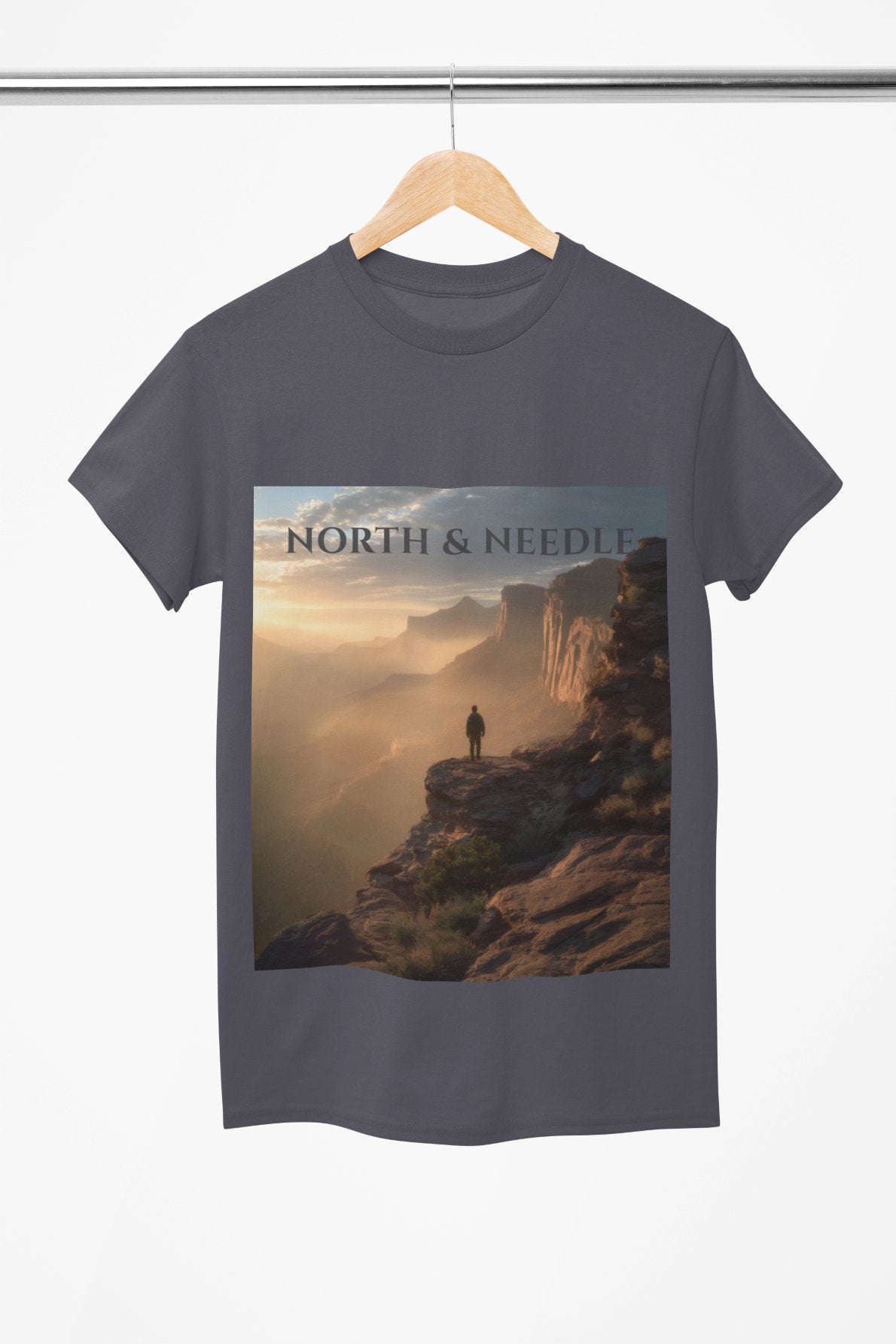 T-shirt with a scenic design of a person on a cliff and 'North & Needle' text, hanging on a wooden hanger.